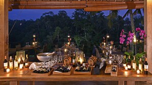 Un área de comedor al aire libre con mesas de madera, botellas de vino, copas y velas.