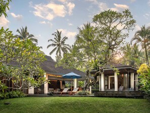 Un resort tropical con una zona de estar cubierta al aire libre, una piscina y abundante vegetación.