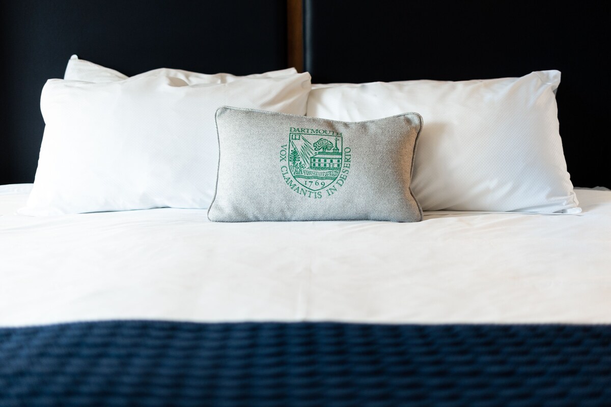 A bed with white bedding and a single pillow featuring a coat of arms.