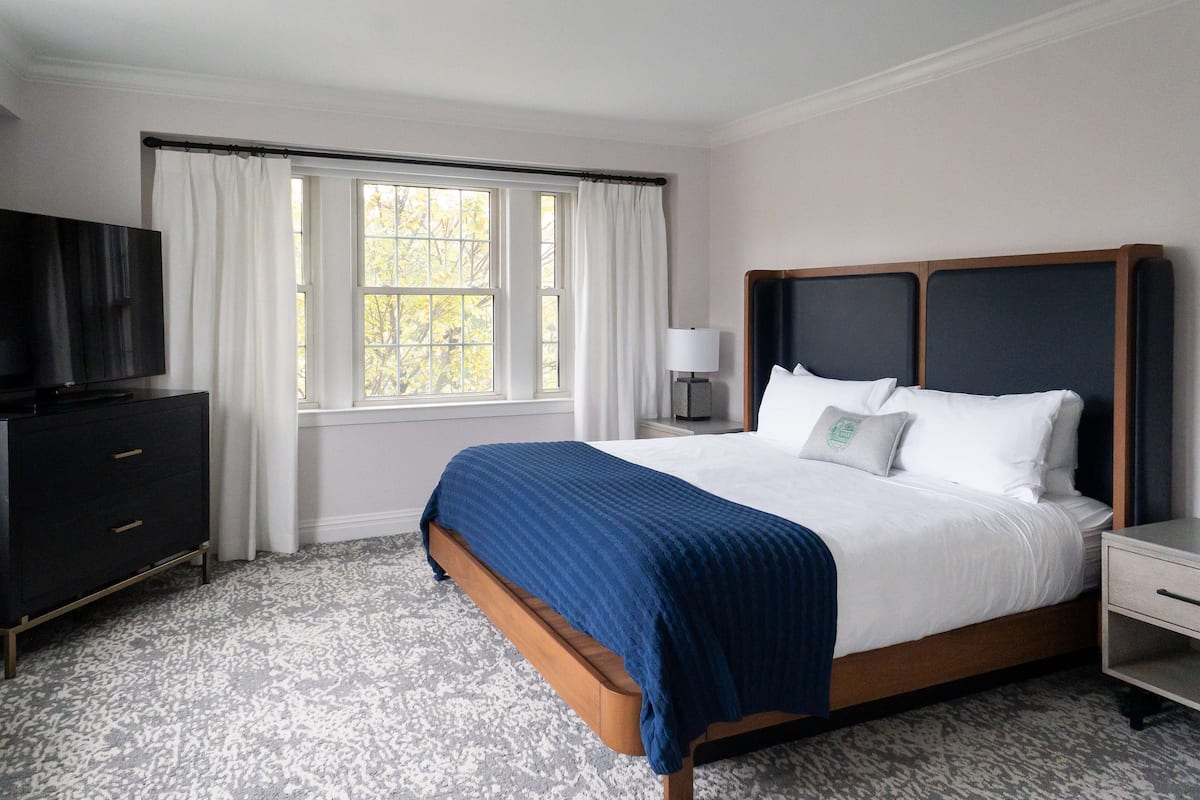 A hotel room with a large bed, a TV, a desk, and a window with curtains.