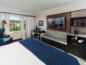A hotel room with a bed, a desk, a chair, a coffee maker, and a painting on the wall.