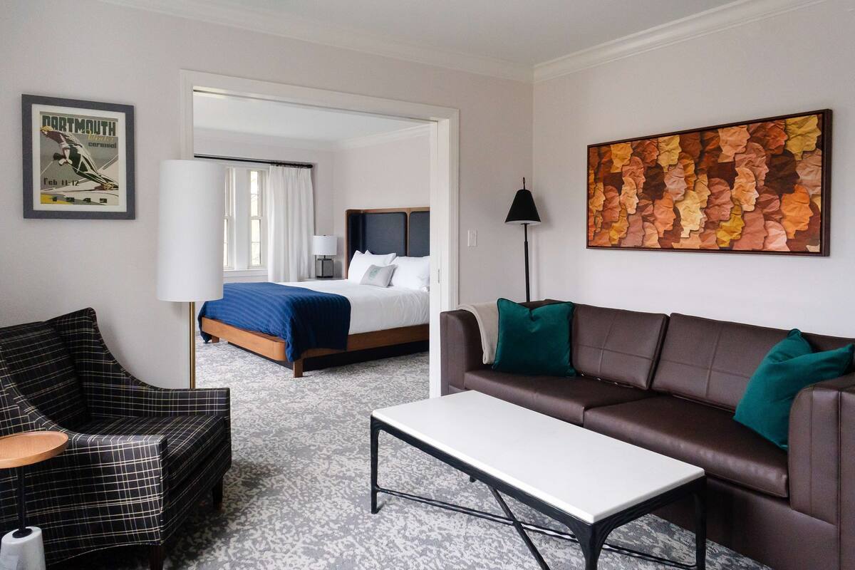 A hotel room with a bed, a sofa, a coffee table, a chair, and a painting on the wall.