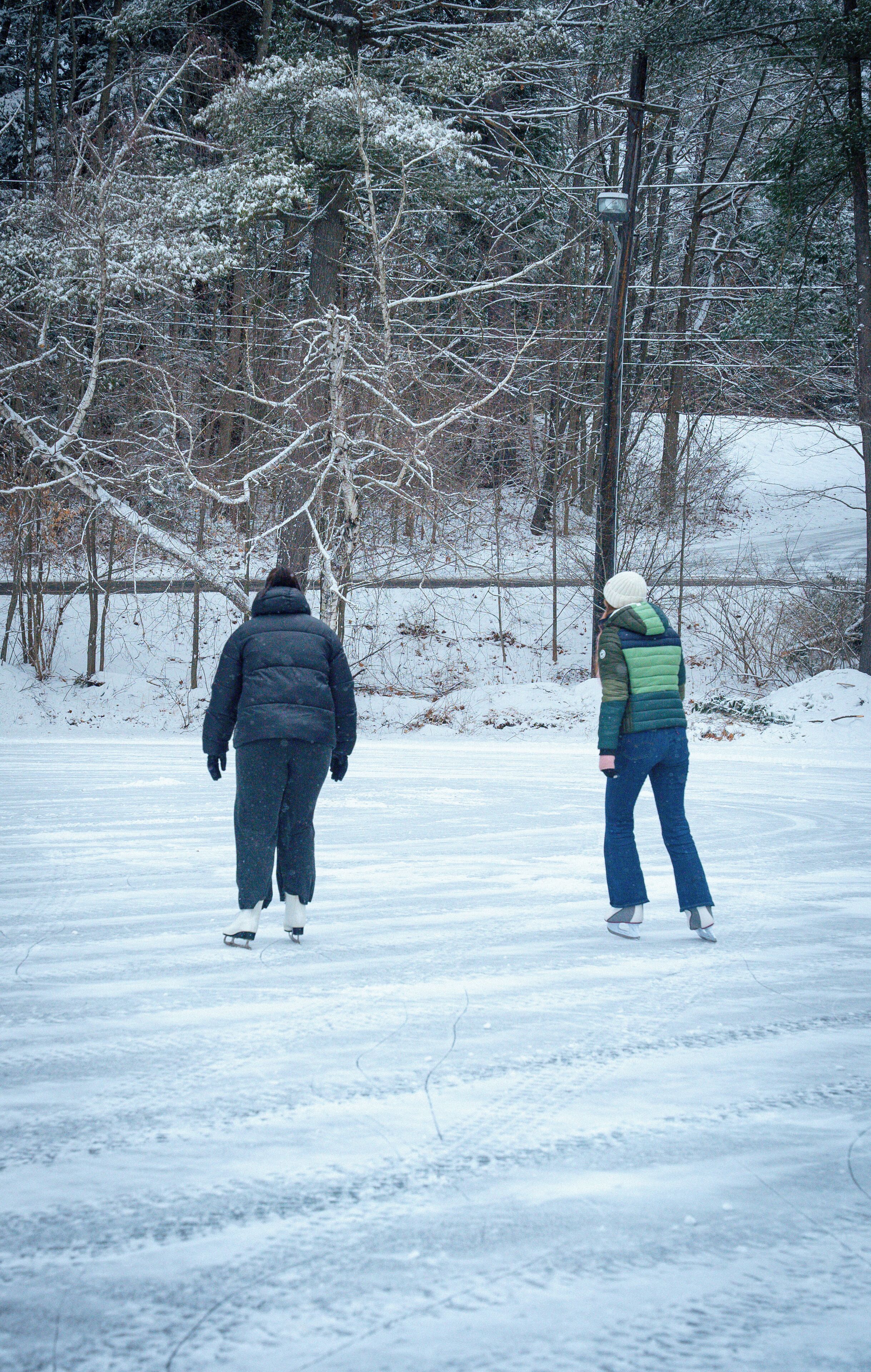 Dos personas patinan sobre hielo en un sendero cubierto de nieve en un área boscosa.