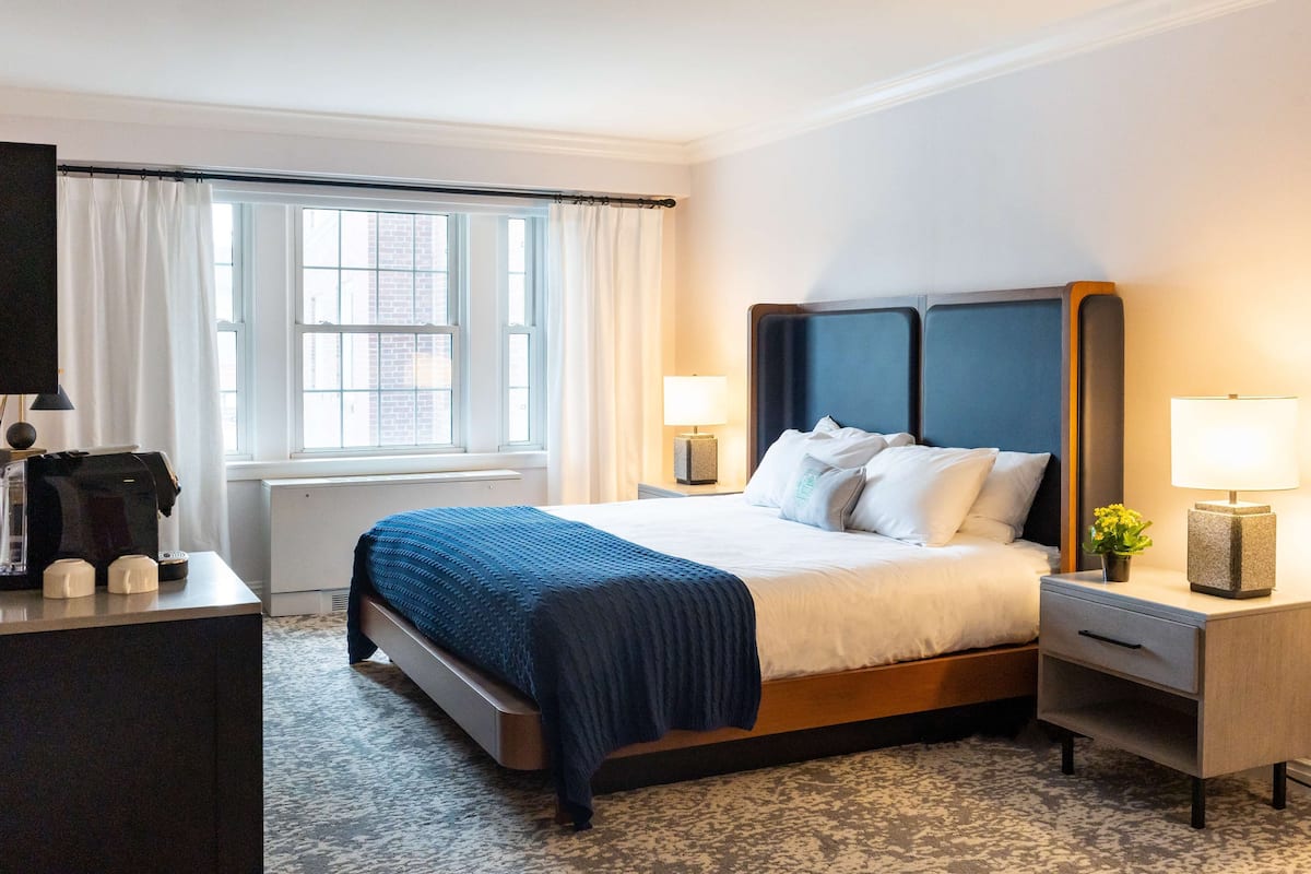 A hotel room with a bed, bedside tables, a desk with a coffee maker, and a window with curtains.