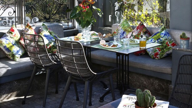Una terraza en la azotea con una mesa lista para comer, rodeada de sillas y macetas con plantas.