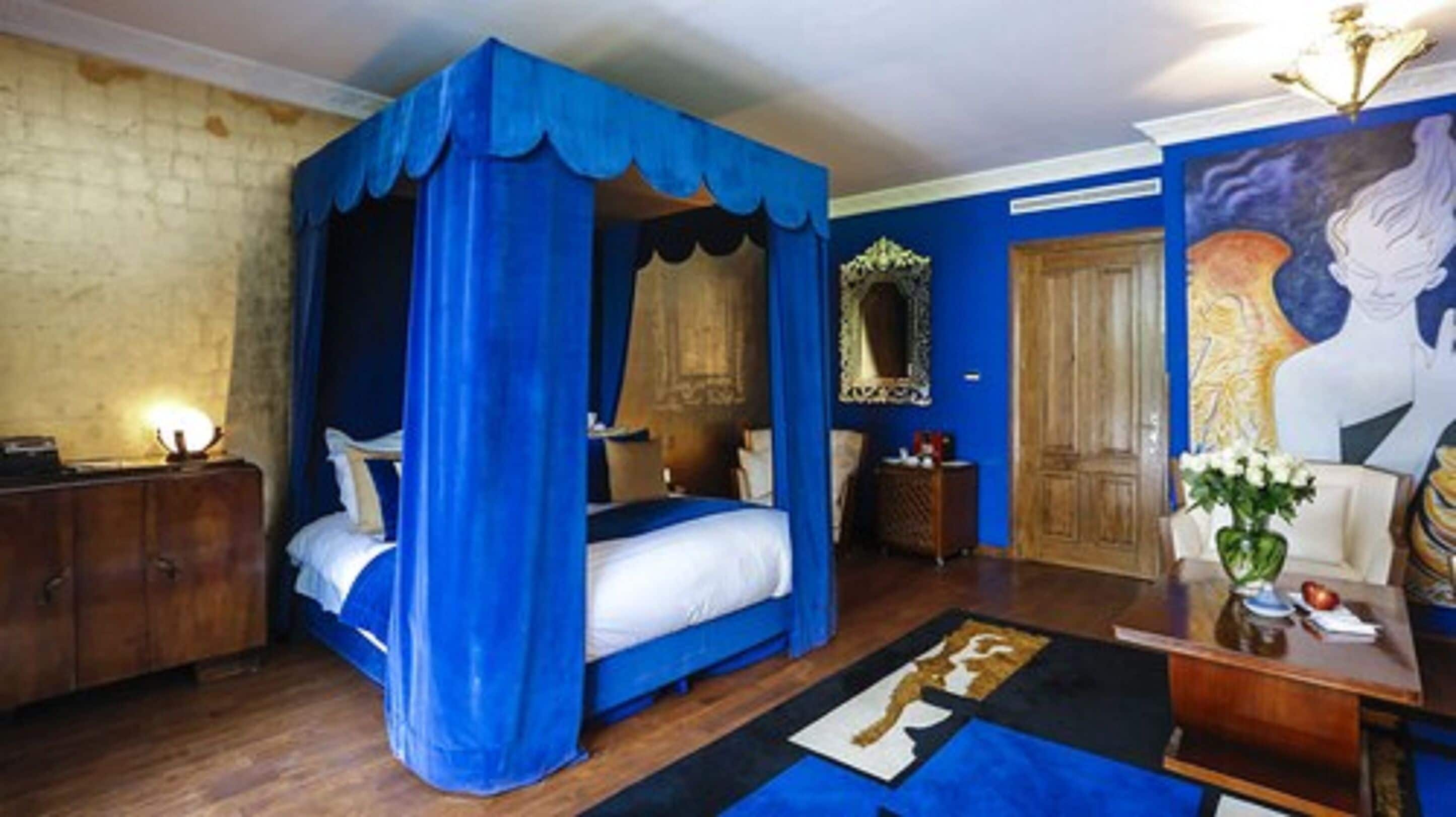 A bedroom with a four-poster bed, a wooden wardrobe, a mirror, and a painting on the wall.