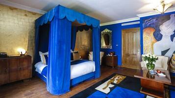 A bedroom with a four-poster bed, a wooden wardrobe, a mirror, and a painting on the wall.