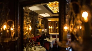 Vista interior de un comedor con mesas dispuestas para comidas, asientos tapizados en rojo y decoraciones ornamentales en las paredes.