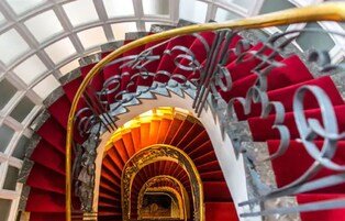 Una imponente escalera con peldaños rojos y barandilla dorada, que conduce a un arco de entrada.