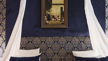 Une chambre à coucher avec un grand lit, un baldaquin, un papier peint à motifs et une œuvre d’art encadrée accrochée au mur.