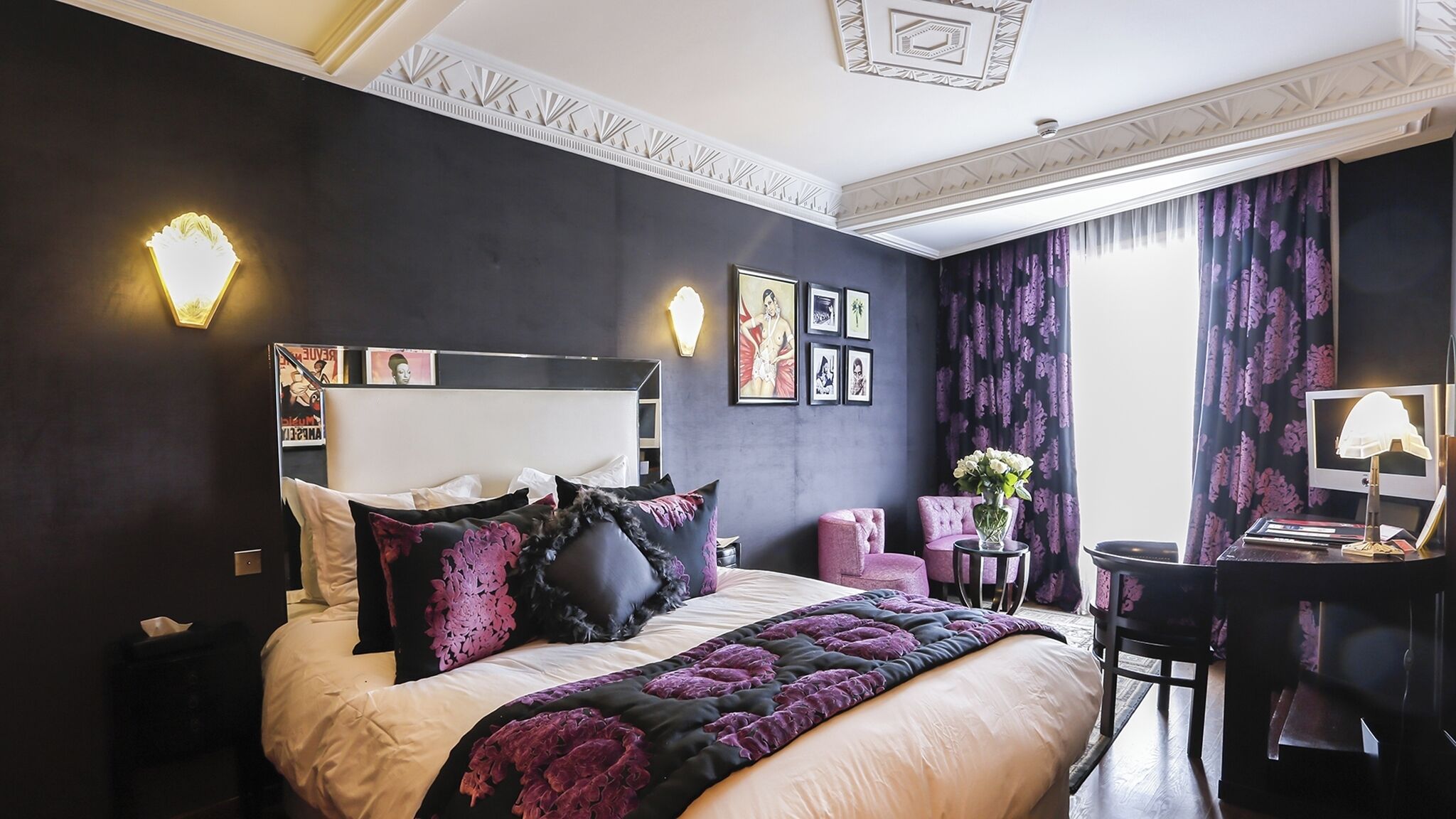 Een slaapkamer met een bed, nachtkastje, lamp en een bureau met stoel.