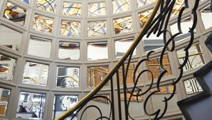 Un interior imponente con un techo circular de vitrales, una escalera central con barandillas negras ornamentadas y múltiples ventanas que dejan entrar luz natural.