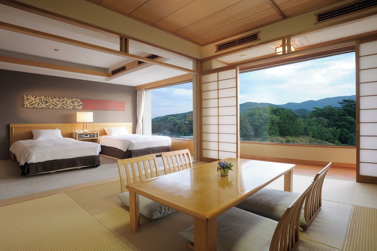 Habitación de hotel con dos camas, una mesa de comedor y vistas a la montaña.