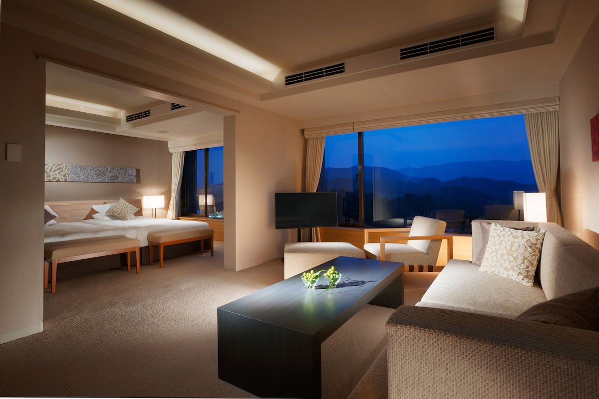 Una habitación de hotel con cama, sofá, mesa de centro y televisor.
