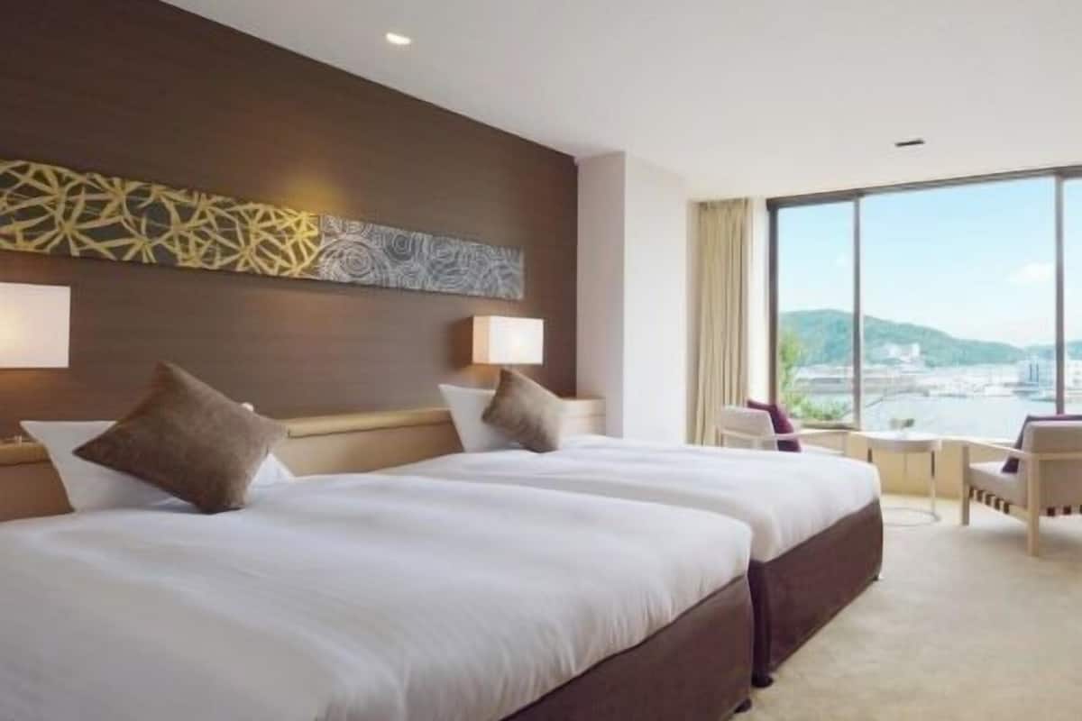 Una habitación de hotel con dos camas, un ventanal con vistas a la ciudad, un escritorio y una silla.