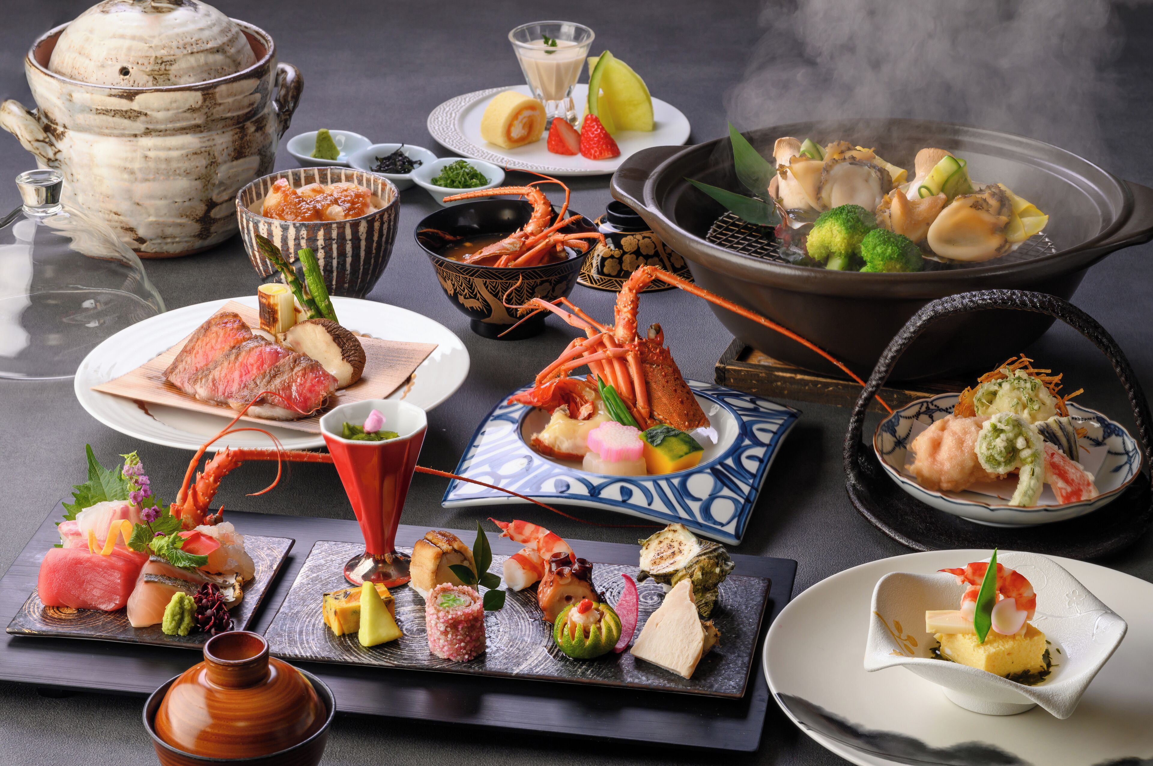 A variety of Japanese dishes including sushi, sashimi, and tempura, served on a table with a teapot and a hot pot.