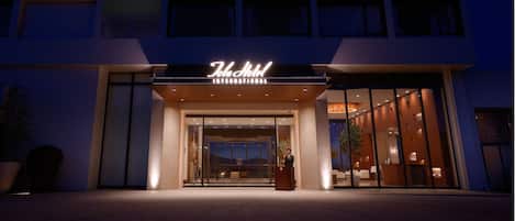 A hotel entrance with a modern design, a reception desk, and a large glass facade.
