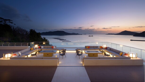 A rooftop terrace with a view of the sea, featuring a long sofa, chairs, and tables with ambient lighting. - Toba Hotel International (Toba)