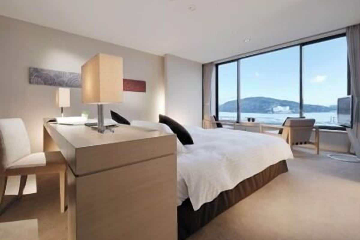 Habitación de hotel moderna con cama, escritorio, silla y ventanas amplias que dan al mar.