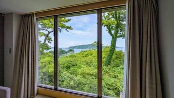 A room with a large window offering a view of a forested area and a distant shoreline.