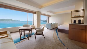 A modern hotel room with a large window offering a sea view, a cozy seating area, a small table, and a minimalist design. - Toba Hotel International (Toba)