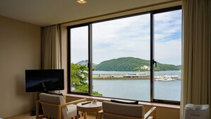 A hotel room with a large window, a bed, two chairs, a small table, a TV, and a heater. - Toba Hotel International (Toba)