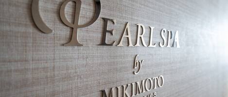 A sign with the text "Pearls Spa by Mikimoto Cosmetics" on a textured fabric background.
