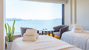 A hotel room with a large window overlooking a body of water, two gray armchairs, a small round table, and a potted plant. - Toba Hotel International (Toba)