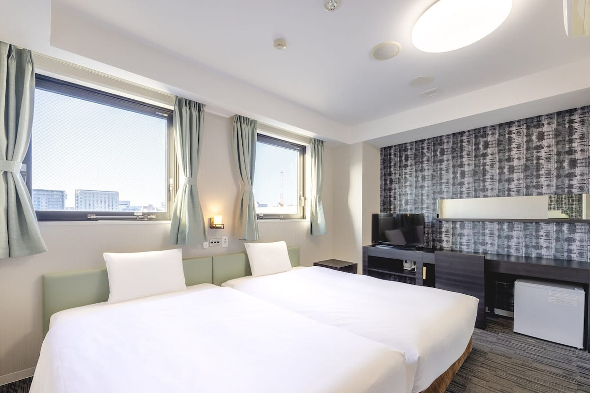 Ein Hotelzimmer mit zwei Betten, einem Schreibtisch und einem Fernseher, mit Blick auf die Stadt.