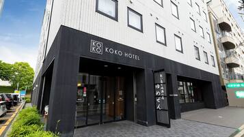 Ein modernes Gebäude mit einem Schild für das Koko Hotel, das einen Glastürbereich und ein schwarzes Markisenverdeck hat.