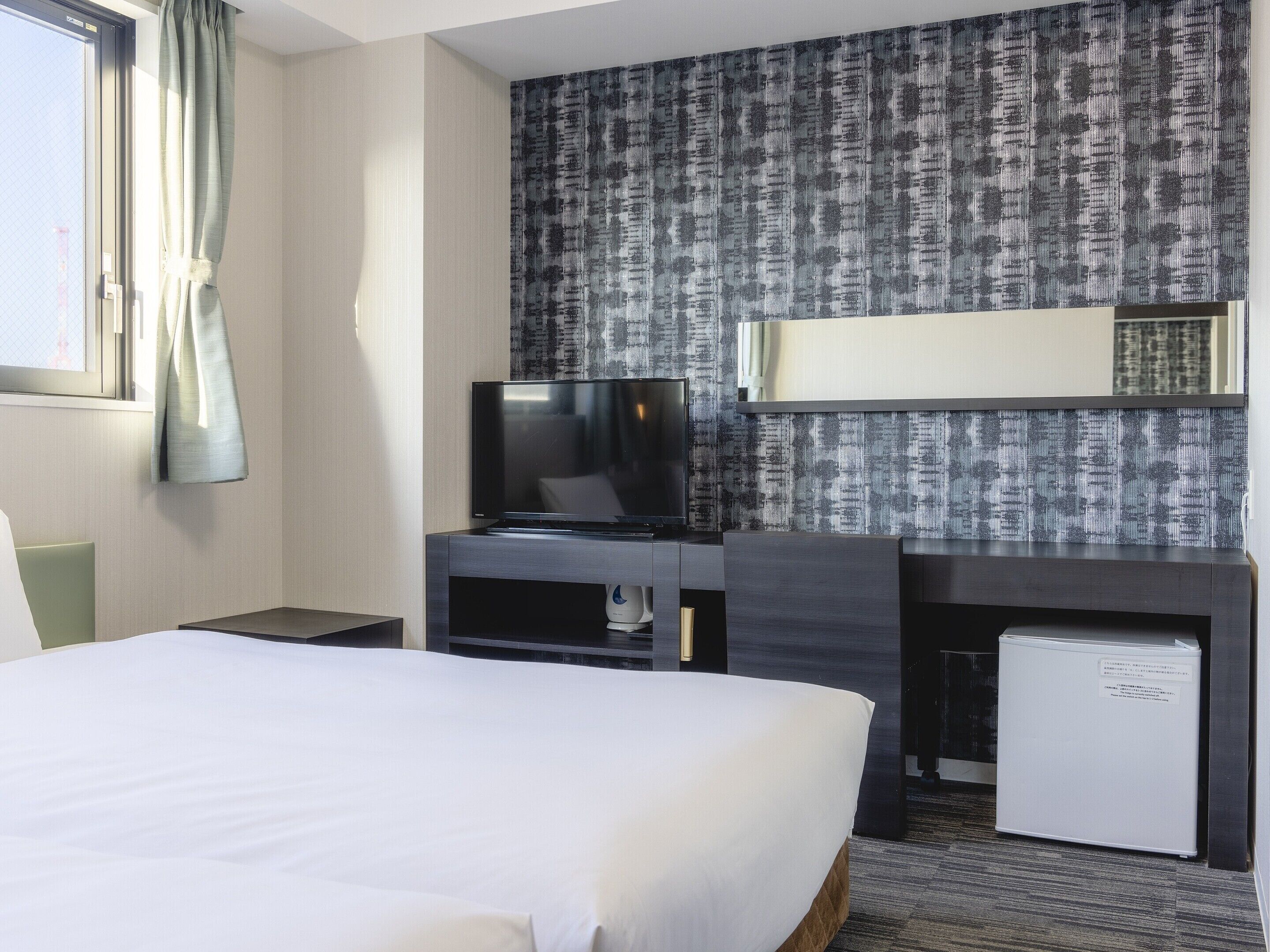 A hotel room with a bed, a television, a small refrigerator, and a mirror on the wall.