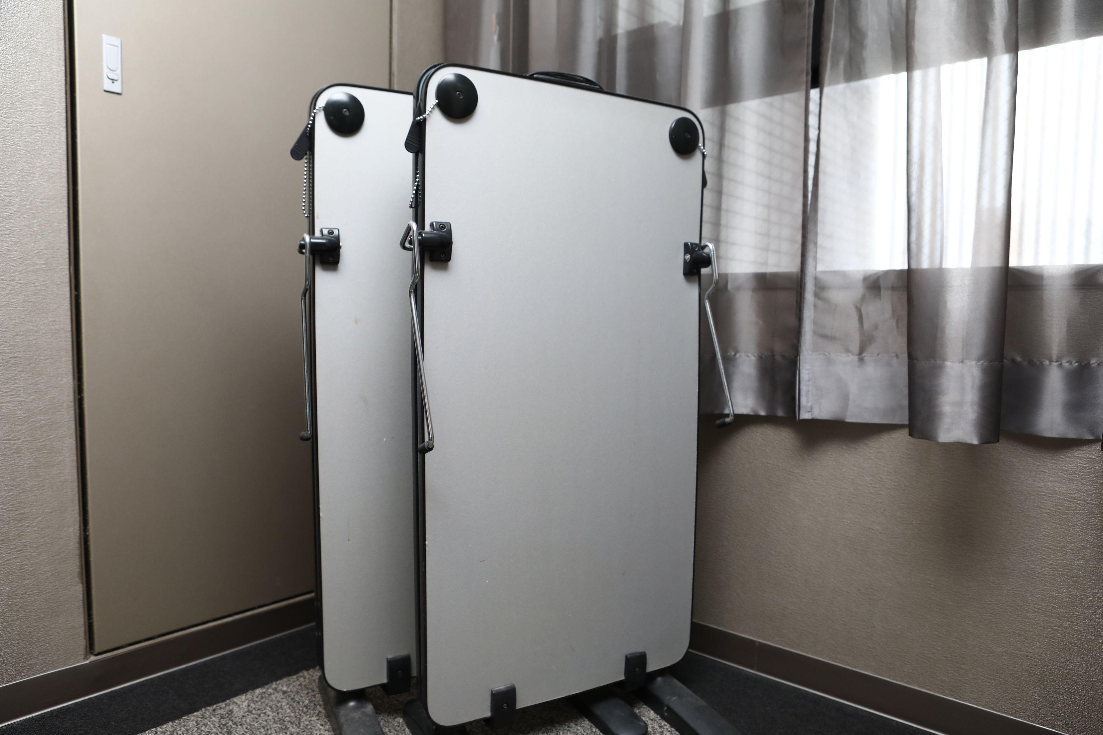Two white portable dividers in a hallway with a striped curtain and a light switch on the wall.