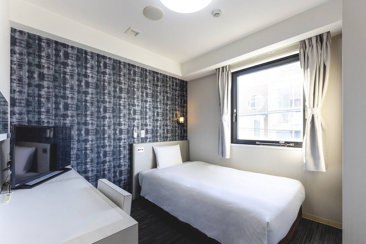 Ein Hotelzimmer mit Bett, Schreibtisch, Spiegel, Fenster mit Vorhängen und einer Wand mit Muster.