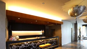 Una moderna zona de recepción con un mostrador de madera, dos taburetes y una pared decorativa con estampado floral.