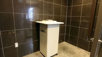 Un baño con paredes de azulejos oscuros, un lavamanos blanco y una zona de ducha.