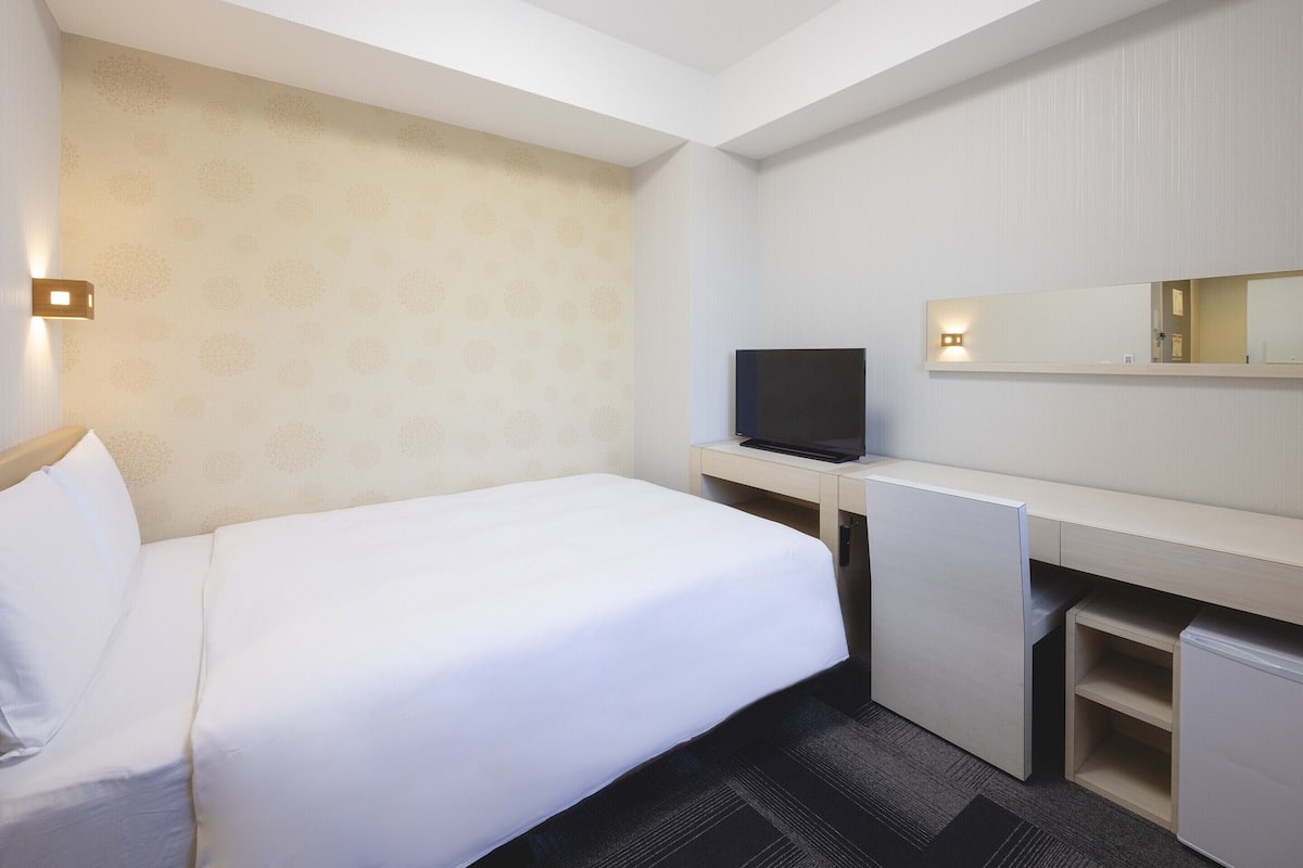 Ein Hotelzimmer mit Bett, Schreibtisch mit Fernseher, Spiegel und einem kleinen Schrank.
