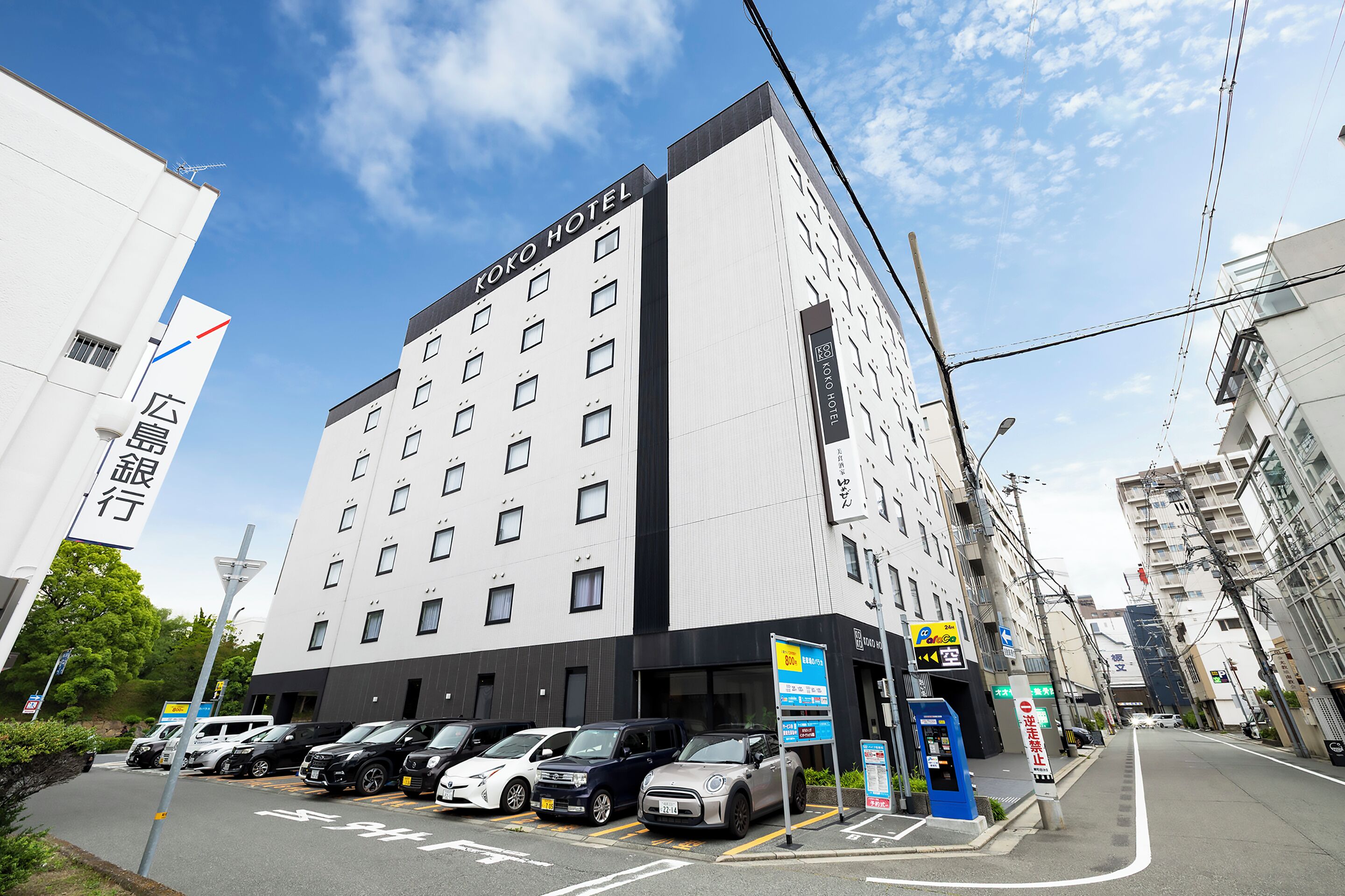 A hotel with multiple floors, a parking lot with several cars, and a clear sky.