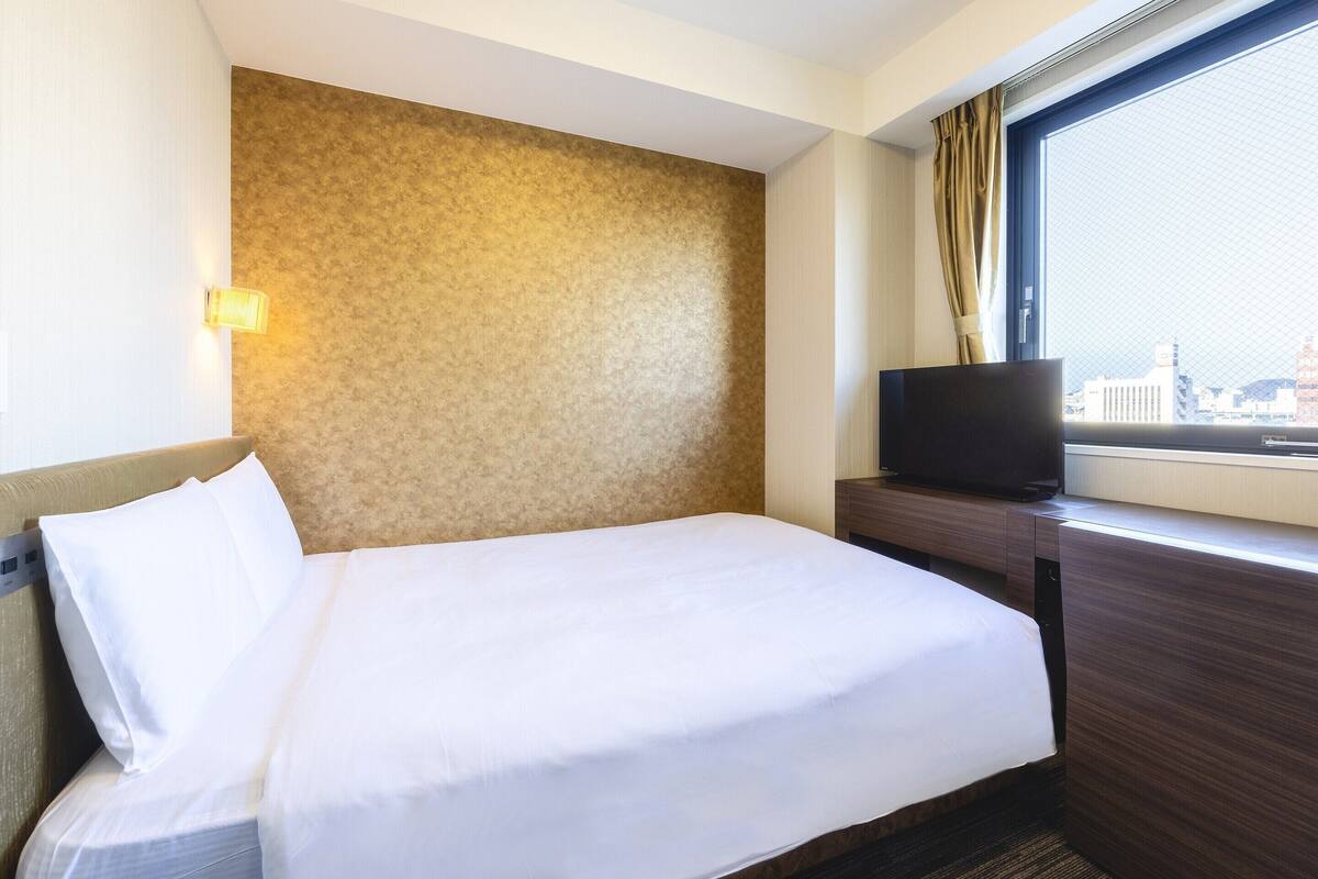 Ein Hotelzimmer mit Bett, Fernseher auf einer Holzkonsole und Fenster mit Blick auf die Stadt.