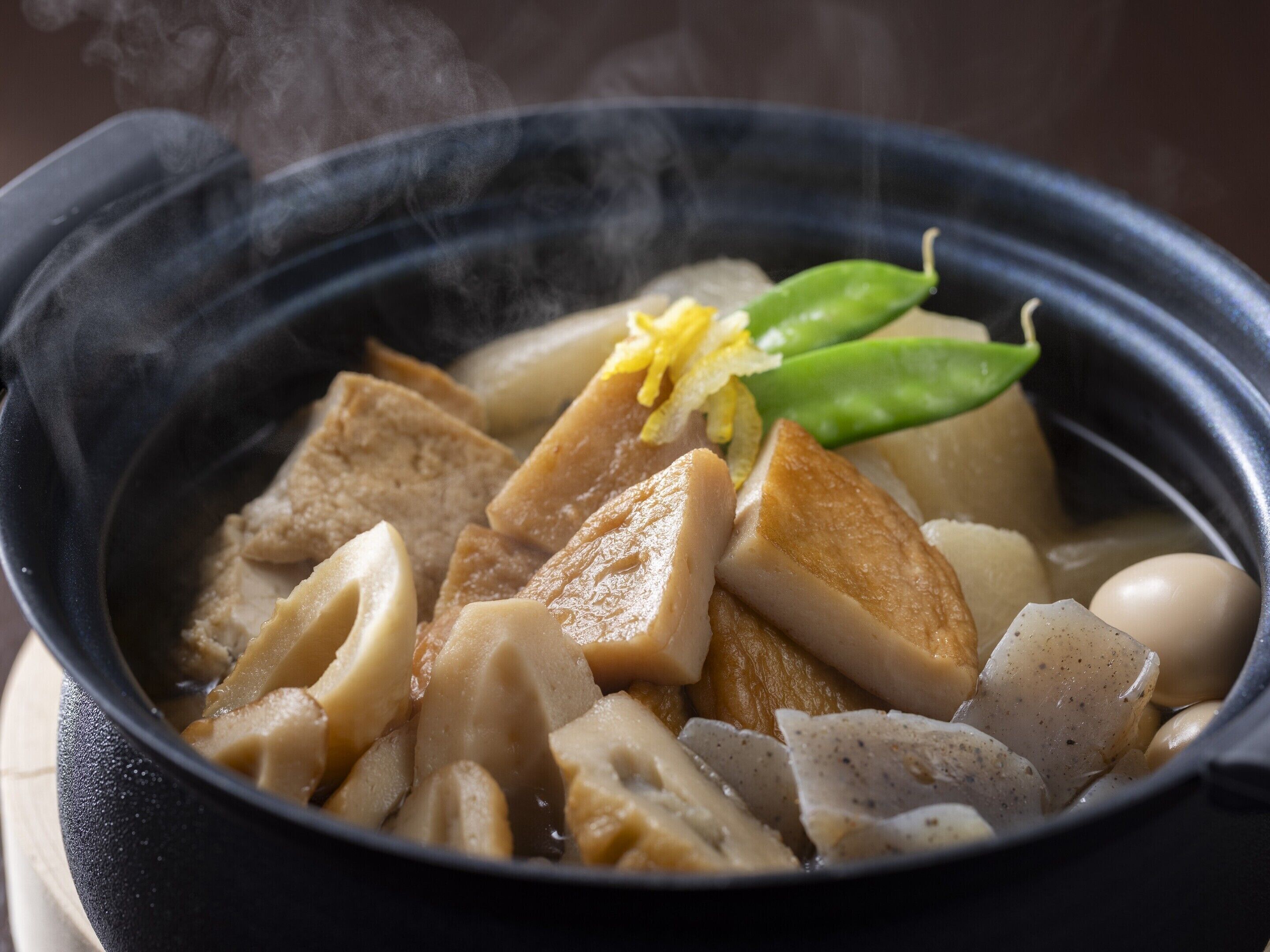 Una olla caliente con tofu, verduras y una ramita de hoja verde como adorno.