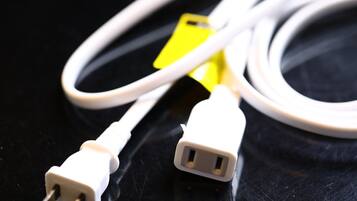 A close-up of a white power cable with a yellow tag and a white USB connector on a black surface.