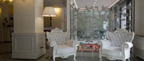 A room with two white upholstered chairs, a decorative glass partition, and a lamp.