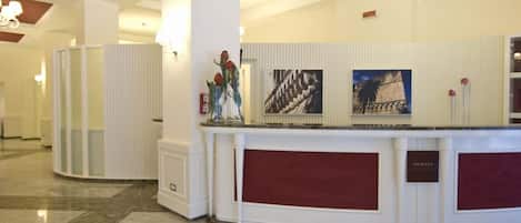 Zona de recepción de un hotel con suelo de mármol, un mostrador y una araña.