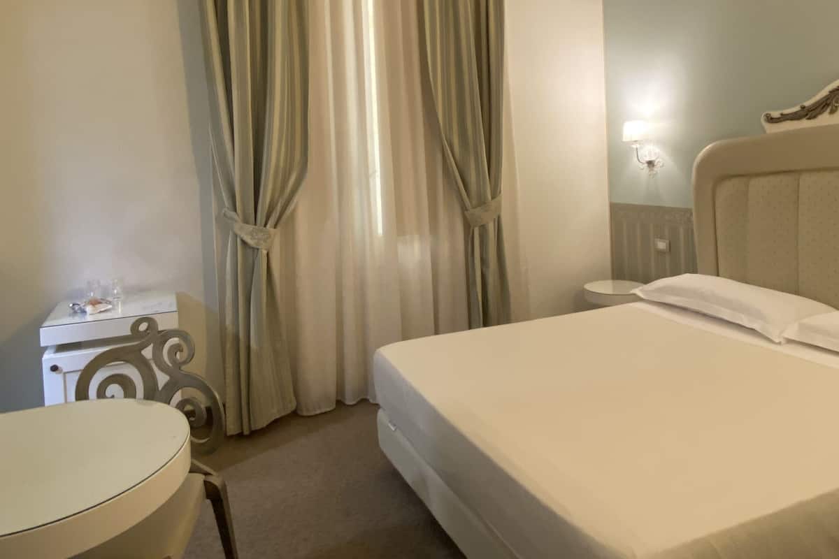 A hotel room with a bed, a small table, a chair, and curtains.