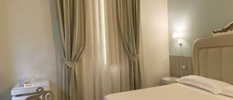 A hotel room with a bed, a small table, a chair, and curtains.
