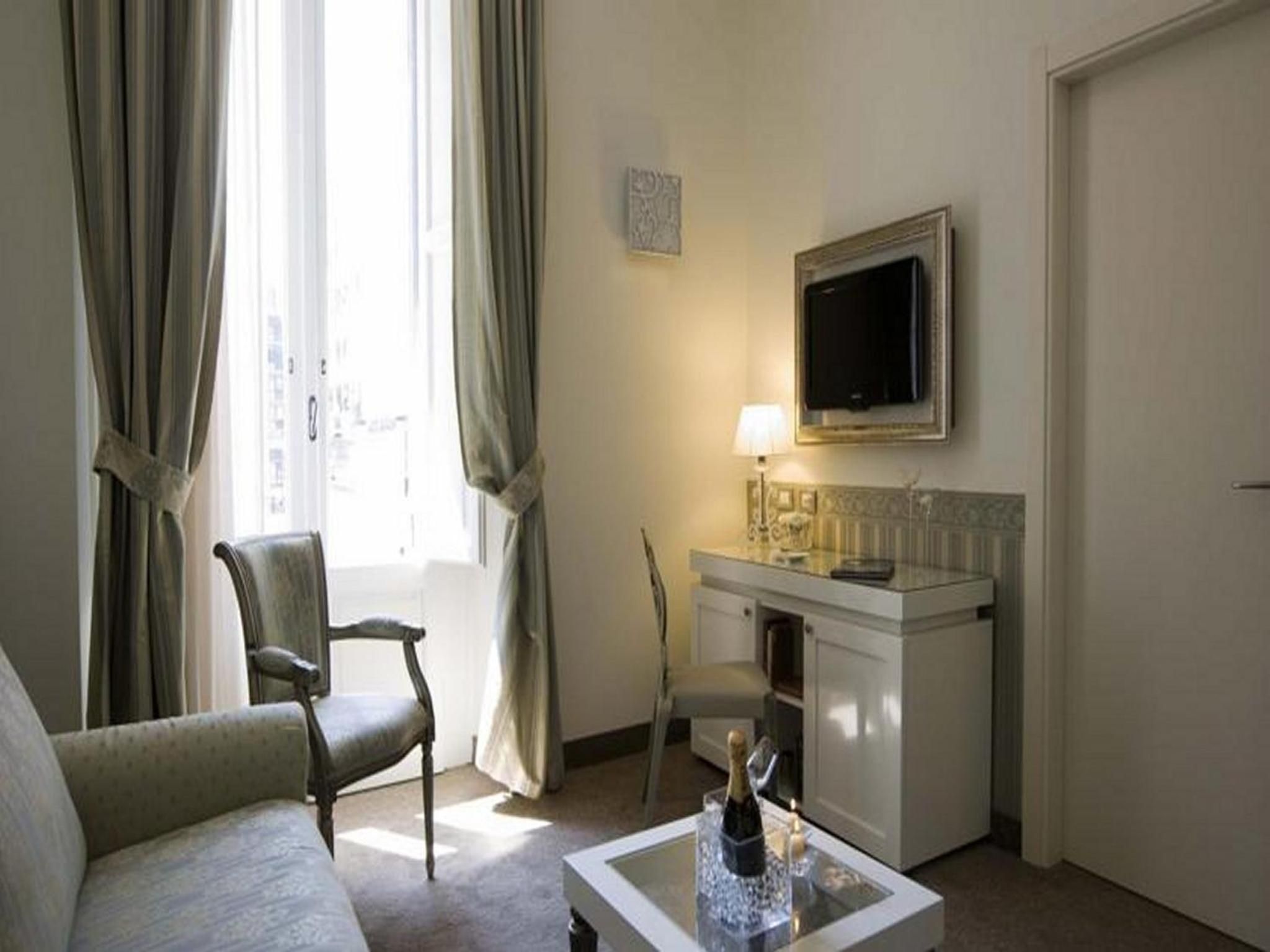 Habitación de hotel con sofá, una silla, una mesita con una botella, televisión y minibar.