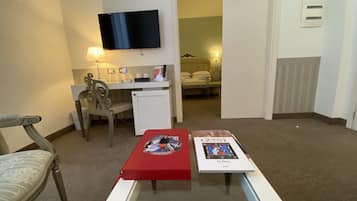Habitación de hotel con escritorio, televisor montado en la pared, cama y una mesita con un libro y una caja roja.