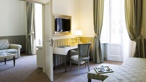 Habitación de hotel con cama, escritorio, silla, televisor y ventana con cortinas.
