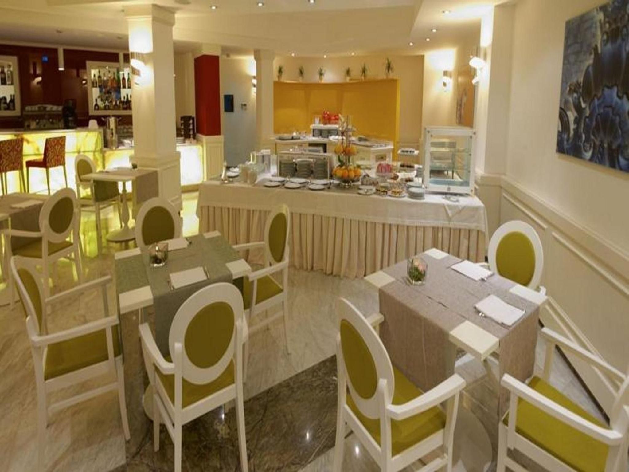 A hotel dining area with round tables, chairs, and a buffet counter.
