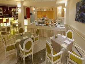 Un espace de restauration d'hôtel avec des tables rondes, des chaises et un buffet.