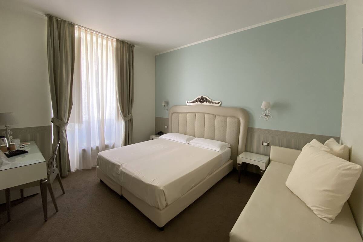 A hotel room with a bed, a desk, a chair, a nightstand, and a sofa.
